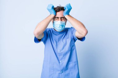 Genç adam stresli ve endişeli, depresyonda ve baş ağrısı yüzünden hayal kırıklığına uğramış hissediyor, iki elini de başa kaldırıyor. Coronavirus konsepti