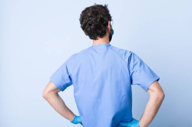 Genç adam kafası karışık ya da dolu hissediyor ya da şüphe ve sorular, merak ediyor, elleri kalçasında, dikiz aynasından bakıyor. Coronavirus konsepti