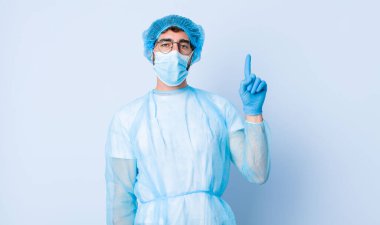 Genç adam mutlu ve mutlu bir şekilde gülümsüyor, tek eliyle yukarıyı göstererek boşluğu kopyalıyor. Coronavirus konsepti