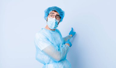 Genç adam şaşkın ve şaşırmış hissediyor, yan taraftaki boşluğu işaret ediyor, şaşkın, açık ağızlı bir bakışla. Coronavirus konsepti