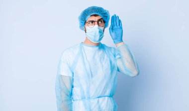 Genç adam ciddi ve meraklı görünüyor, dinliyor, gizli bir konuşma veya dedikodu duymaya çalışıyor, kulak misafiri oluyor. Coronavirus konsepti