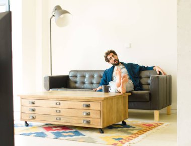 Oturma odasında kanepede oturup televizyon ya da bilgisayar izleyen genç havalı bir adam.