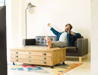 Oturma odasında kanepede oturup televizyon ya da bilgisayar izleyen genç havalı bir adam.