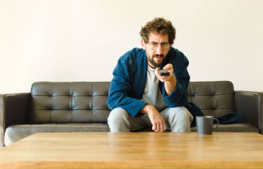 Oturma odasında kanepede oturup televizyon ya da bilgisayar izleyen genç havalı bir adam.