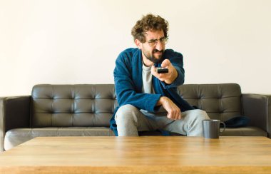 Oturma odasında kanepede oturup televizyon ya da bilgisayar izleyen genç havalı bir adam.