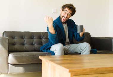 Oturma odasında kanepede oturup televizyon ya da bilgisayar izleyen genç havalı bir adam.