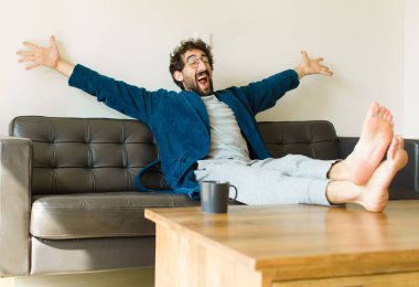 Oturma odasında kanepede oturup televizyon ya da bilgisayar izleyen genç havalı bir adam.