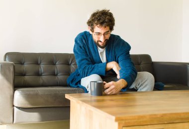 Oturma odasında kanepede oturup televizyon ya da bilgisayar izleyen genç havalı bir adam.