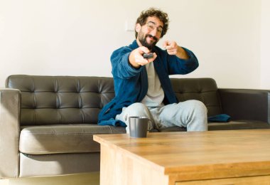 Oturma odasında kanepede oturup televizyon ya da bilgisayar izleyen genç havalı bir adam.