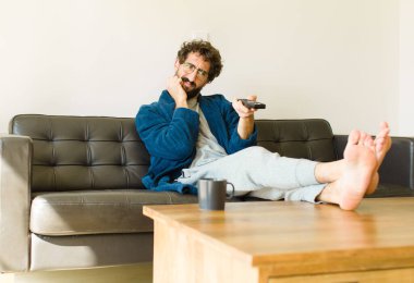Oturma odasında kanepede oturup televizyon ya da bilgisayar izleyen genç havalı bir adam.