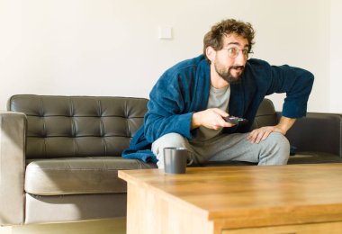 Oturma odasında kanepede oturup televizyon ya da bilgisayar izleyen genç havalı bir adam.