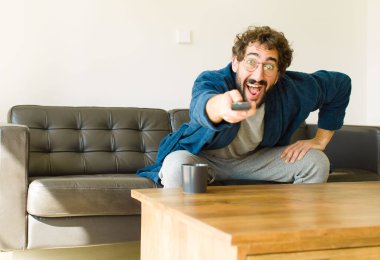 Oturma odasında kanepede oturup televizyon ya da bilgisayar izleyen genç havalı bir adam.