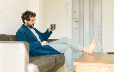 Oturma odasında kanepede oturup televizyon ya da bilgisayar izleyen genç havalı bir adam.