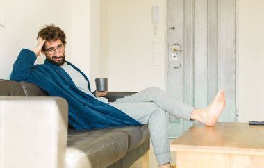 Oturma odasında kanepede oturup televizyon ya da bilgisayar izleyen genç havalı bir adam.