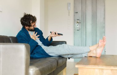 Oturma odasında kanepede oturup televizyon ya da bilgisayar izleyen genç havalı bir adam.