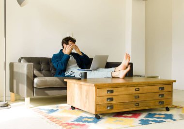 Oturma odasında kanepede oturup televizyon ya da bilgisayar izleyen genç havalı bir adam.