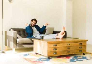 Oturma odasında kanepede oturup televizyon ya da bilgisayar izleyen genç havalı bir adam.