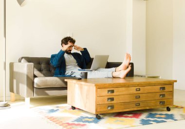 Oturma odasında kanepede oturup televizyon ya da bilgisayar izleyen genç havalı bir adam.