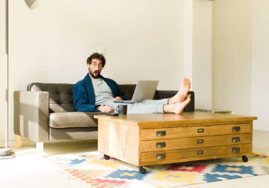 Oturma odasında kanepede oturup televizyon ya da bilgisayar izleyen genç havalı bir adam.