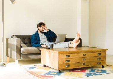 Oturma odasında kanepede oturup televizyon ya da bilgisayar izleyen genç havalı bir adam.