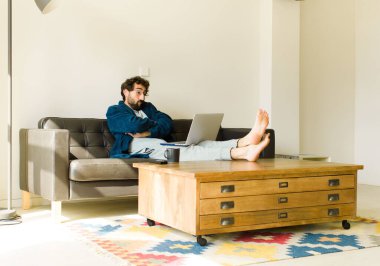 Oturma odasında kanepede oturup televizyon ya da bilgisayar izleyen genç havalı bir adam.