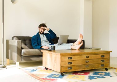 Oturma odasında kanepede oturup televizyon ya da bilgisayar izleyen genç havalı bir adam.