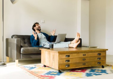 Oturma odasında kanepede oturup televizyon ya da bilgisayar izleyen genç havalı bir adam.