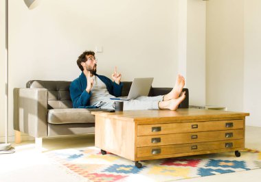 Oturma odasında kanepede oturup televizyon ya da bilgisayar izleyen genç havalı bir adam.