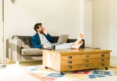 Oturma odasında kanepede oturup televizyon ya da bilgisayar izleyen genç havalı bir adam.