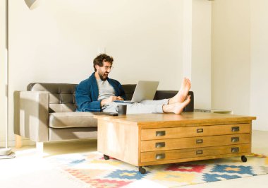 Oturma odasında kanepede oturup televizyon ya da bilgisayar izleyen genç havalı bir adam.