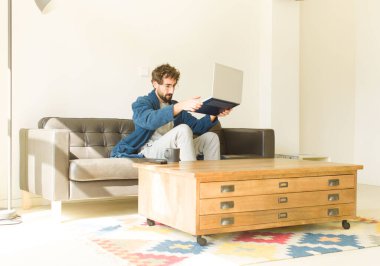 Oturma odasında kanepede oturup televizyon ya da bilgisayar izleyen genç havalı bir adam.