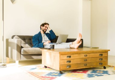 Oturma odasında kanepede oturup televizyon ya da bilgisayar izleyen genç havalı bir adam.