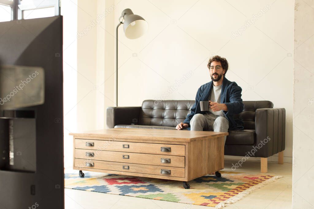 young cool man sitting on a sofa at living room watching tv or computer