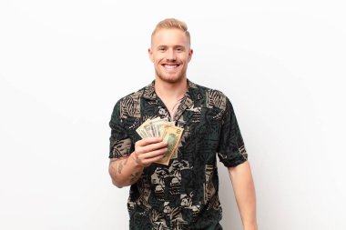 Genç sarışın adam mutlu ve hoş bir şekilde şaşırmış görünüyor. Banknotlarla büyülenmiş ve şok olmuş bir ifadeyle heyecanlanıyor.