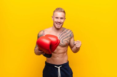 Genç sarışın güçlü adam şok olmuş, heyecanlı ve mutlu hissediyor, gülüyor ve başarıyı kutluyor, vay canına! Boks eldivenleriyle