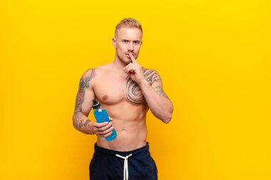 Genç sarışın güçlü adam ciddi görünüyor ve parmaklarını dudaklarına bastırıp sessizlik ya da sessizlik talep ediyor enerji içeceğiyle sır saklıyor.