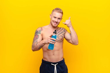 Genç sarışın güçlü adam neşeyle gülümsüyor ve kamerayı işaret ediyor. Daha sonra seni arayıp, bir enerji içeceğiyle telefonla konuşuyor.