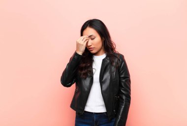 Genç Latin güzel kadın stresli, mutsuz ve hayal kırıklığına uğramış, alnına dokunuyor ve düz duvara karşı şiddetli baş ağrısı çekiyor.