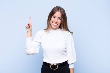 Genç, güzel İspanyol kadın neşeyle ve mutlulukla gülümsüyor, tek eliyle yukarıya bakıyor mavi duvara uzayı kopyalamak için.