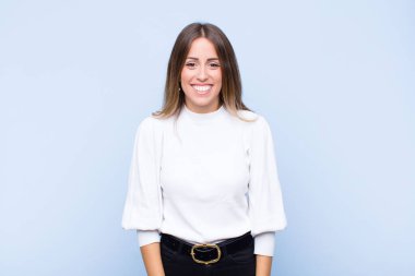 Genç, güzel İspanyol bir kadın mutlu ve şapşal görünüyor. Geniş, eğlenceli, kaçık bir gülüşü ve mavi duvarda gözleri açık.