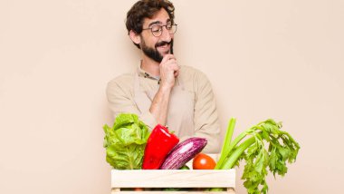 yeşil bakkal adam mutlu, kendinden emin bir ifadeyle gülümsüyor, elleri çenesinde, merak ediyor ve yan tarafa bakıyor.