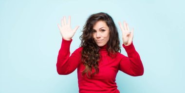 Genç, güzel bir kadın gülümsüyor ve dost canlısı görünüyor. 9 ya da 9 numarayı gösteriyor. Eli önde, mavi duvara doğru sayıyor.