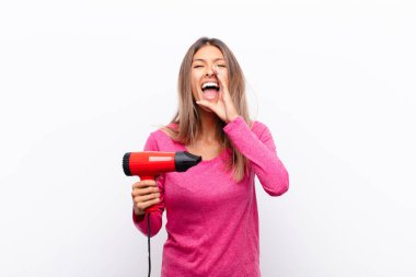Genç, güzel bir kadın mutlu, heyecanlı ve pozitif hissediyor. Elleri ağızda, saç kurutma makinesiyle bağırıyor..