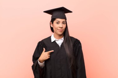 Genç Latin kız öğrenci gururlu, kendinden emin ve mutlu görünüyor, gülümsüyor ve kendini işaret ediyor ya da bir numara işareti yapıyor.