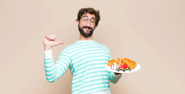 young cool man with waffles against flat wall.