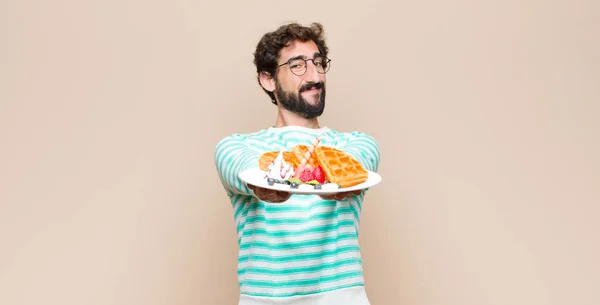 young cool man with waffles against flat wall.