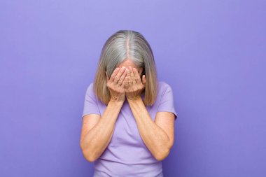 Yaşlı ya da orta yaşlı güzel bir kadın üzgün, hayal kırıklığına uğramış, gergin ve depresif, iki eliyle yüzünü kaplayan, ağlayan