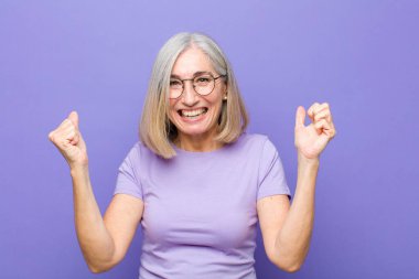 Yaşlı ya da orta yaşlı güzel bir kadın mutlu, pozitif ve başarılı hissediyor, zaferi, başarıları ya da iyi şansı kutluyor.