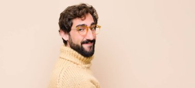 Genç havalı adam mutlu ve neşeli hissediyor, gülümsüyor ve seni selamlıyor, düz duvara karşı dostça bir jestle içeri davet ediyor.