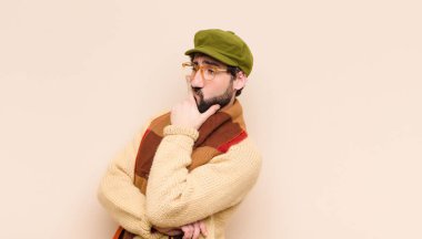 Genç havalı sakallı adam ciddi, düşünceli ve güvensiz görünüyor, bir kolu çapraz ve çenesi üzerinde, seçenekleri tartıyor.